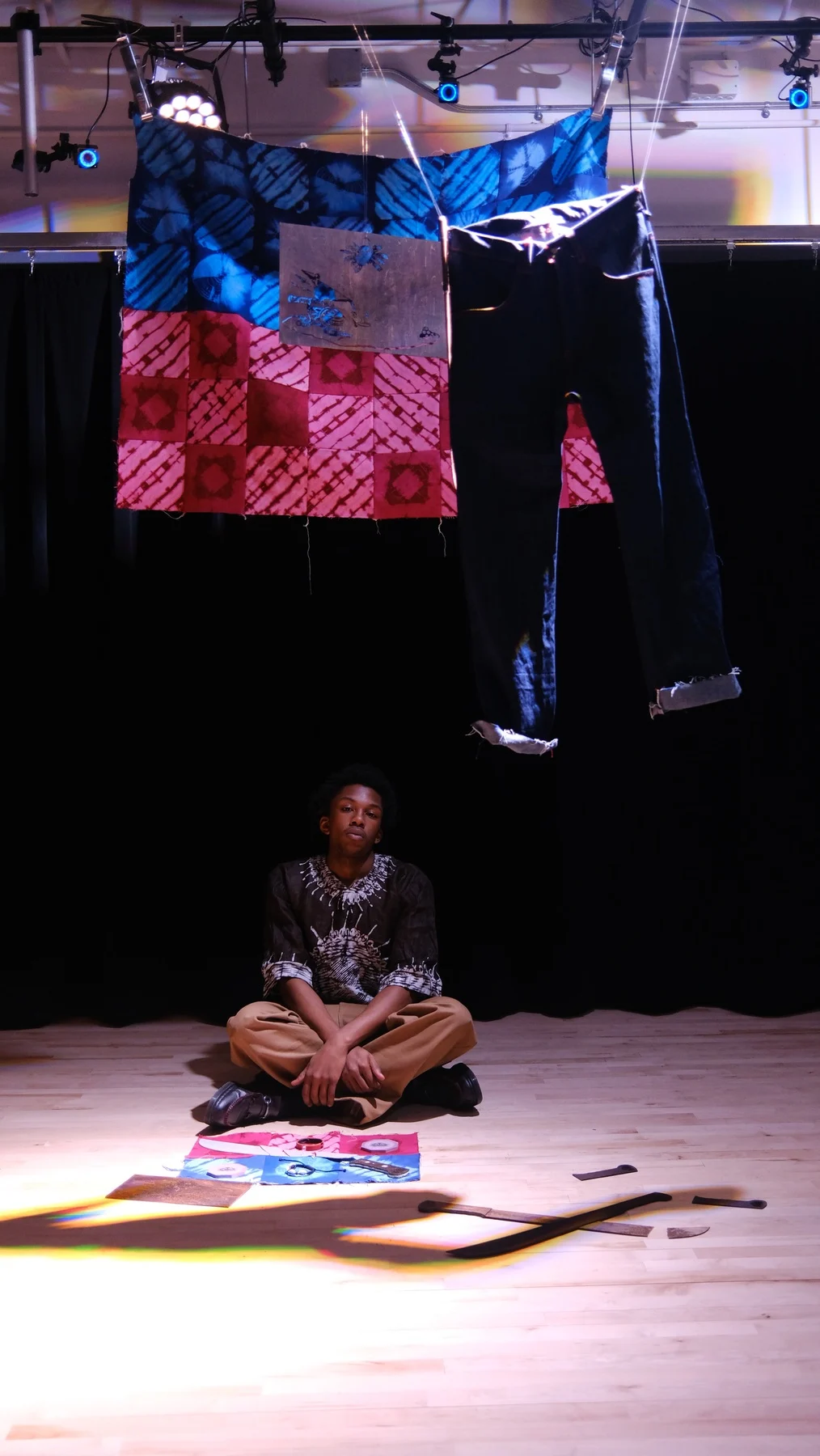 Didier seated beneath textiles and garments in the Bwa Kayiman installation