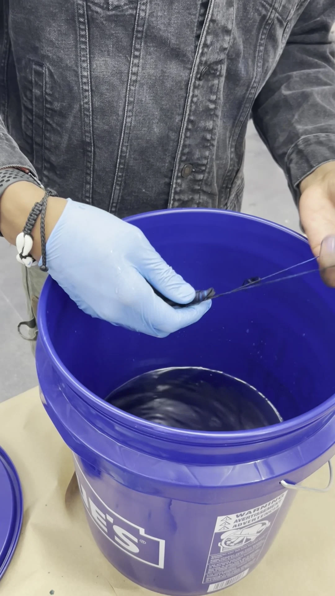 Hands working with a dark textile over a blue dye bucket